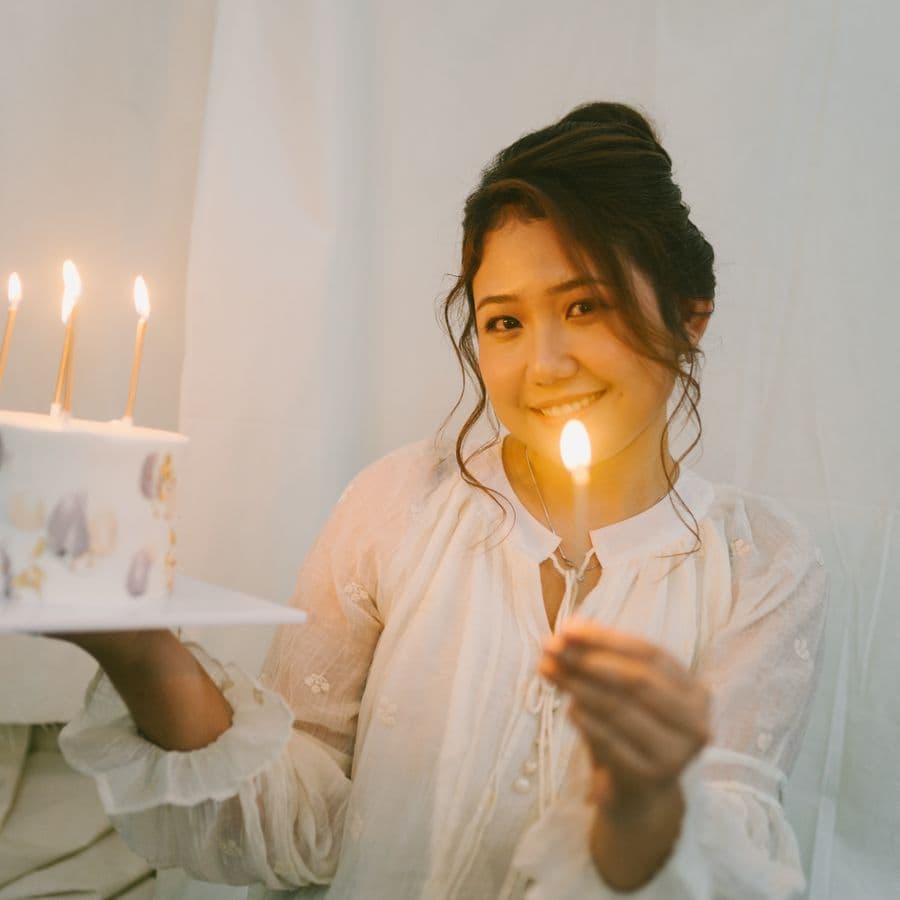 Woman smiling softly while holding a candle-lit birthday cake
