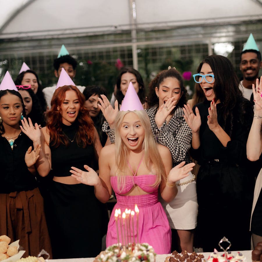 Birthday guest beaming as friends cheer around the cake table