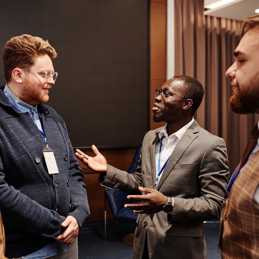 Three professionals in business attire talking with conference lanyards
