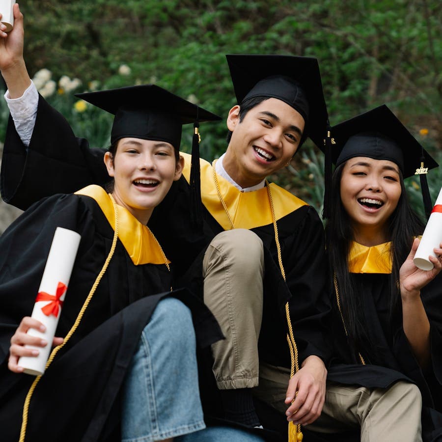 Four graduates in caps and gowns holding diplomas with confetti