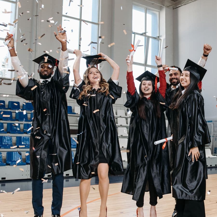 Graduates cheering with arms raised under falling confetti