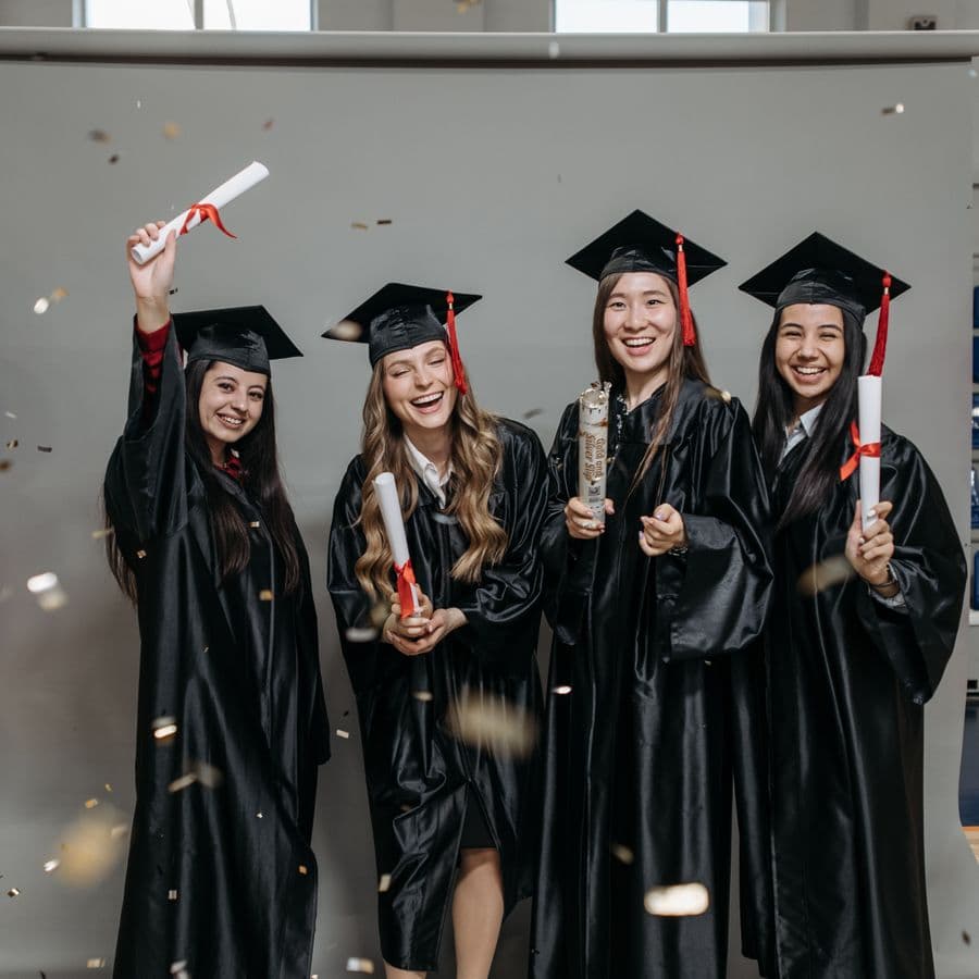 Four women graduates laughing with diplomas and confetti