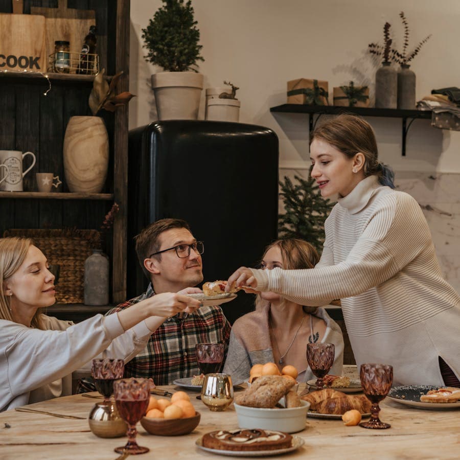 Friends passing food around a cozy holiday dinner table