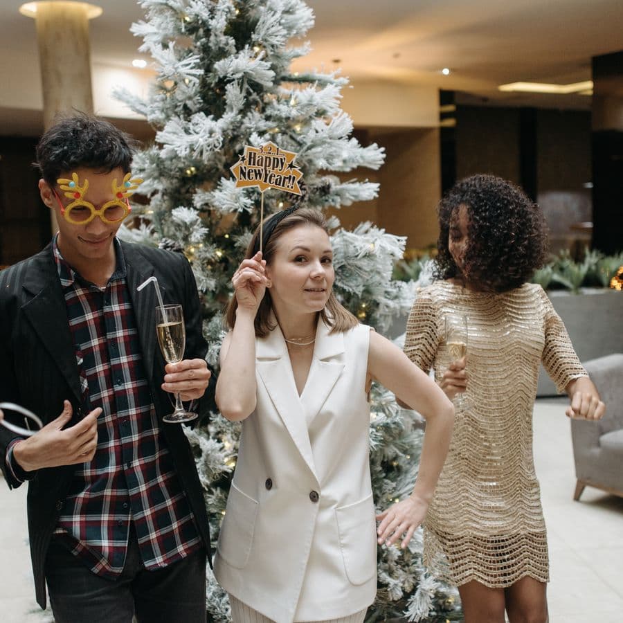 Partygoers holding a Happy New Year prop by the tree