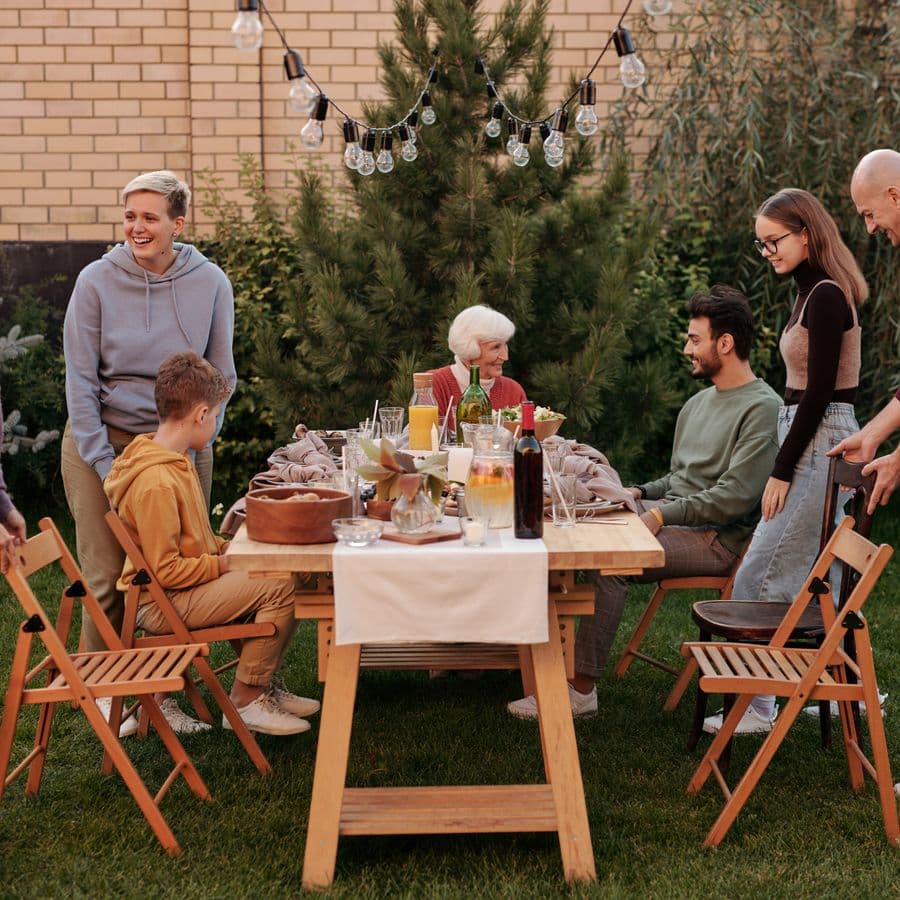 Family sharing a meal at a long backyard table with string lights