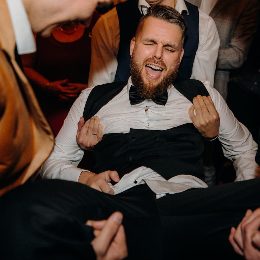 Groom lifted by laughing friends at the reception